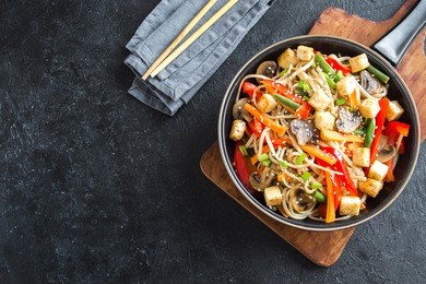 stir fry with udon noodles, tofu, mushrooms and vegetables. asian vegan vegetarian food, meal, stir fry in wok over black background, copy space.