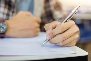 soft focus.high school or university student holding pencil writing on paper answer sheet.sitting on lecture chair taking final exam attending in examination room or classroom.student in casual