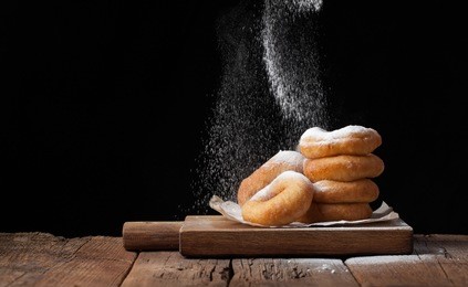 baker sprinkles sweet donuts with powder sugar on black background. delicious, but unhealthy food on the old wooden table with copy space