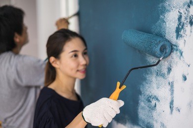young asian couple painting interior wall with paint roller in new house