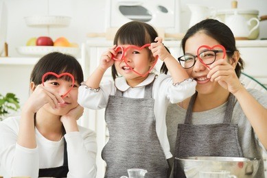 happy asian family holding red hearts shape while baking cookies and cakes in the kitchen together.