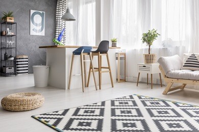 open space living room interior with geometric carpet and dining area with barstools and white bin