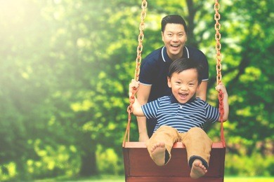 image of young father pushing his son on the swing while having fun in the park