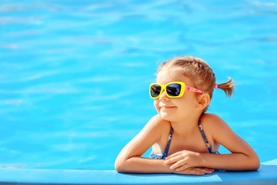 smiling cute little girl in sunglasses in pool in sunny day.
