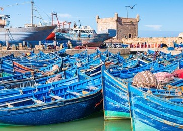 bright blue boats of moroccan fishermen in essaouira port in morocco with fishing nets and ancient fort on background soft focus