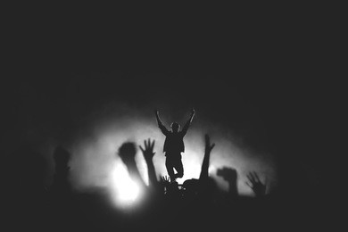 black and white photo of frontman in a stage backlights with hands raised up to the crowd