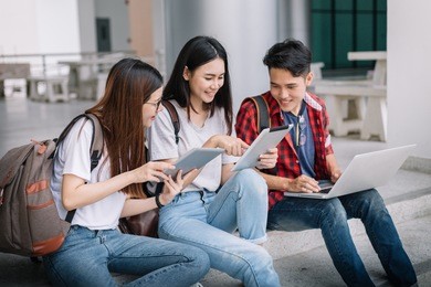 happy group of attractive young people using a laptop and tablet, sitting on study table, social media online and education concept.
