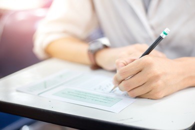 soft focus.high school or university student holding pencil writing on paper answer sheet.sitting on lecture chair taking final exam attending in examination room or classroom.student in casual