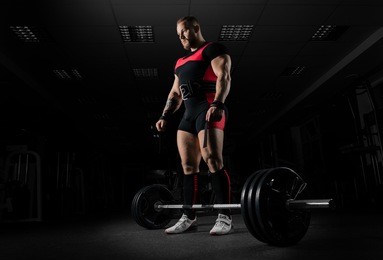 the weightlifter is preparing to perform an exercise called deadlift. he stands directly above the barbell and looks at it.