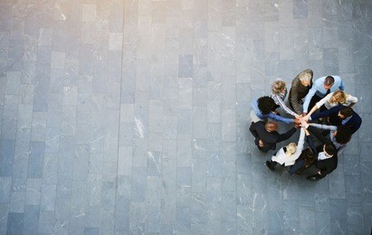 high angle view of a team of united businesspeople standing with their hands together in a huddle in the lobby of a modern office building