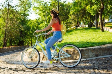 young beautiful woman riding on bicycle in summer park. green trees background 