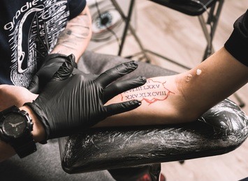 tattoo artist holding a tattoo machine in black sterile gloves. master tattoo draws paint on the clients tattoo.
