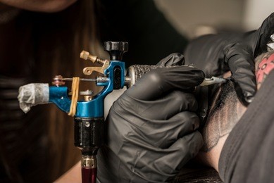 tattoo artist holding a tattoo machine in black sterile gloves. master tattoo draws paint on the clients tattoo.
