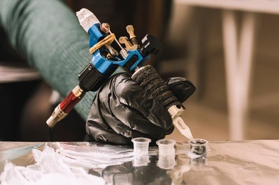tattoo artist holding a tattoo machine in black sterile gloves. master tattoo draws paint on the clients tattoo.