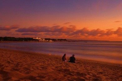 a couple are sitting at the kuta beach bali enjoying the evening sunset