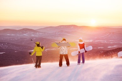group of three friends at ski resort against sunset