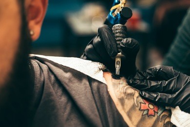 tattoo artist holding a tattoo machine in black sterile gloves. master tattoo draws paint on the clients tattoo.