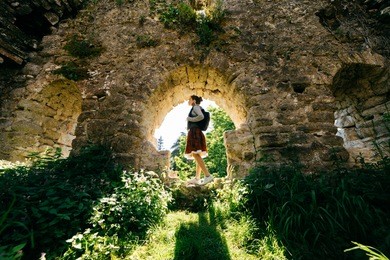 young girl traveler, standing in an ancient abandoned building surrounded by greenery