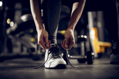 close up front view of woman's hands tying shoelaces on sneakers in the gym.
