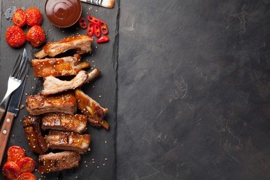 pork ribs in barbecue sauce and honey roasted tomatoes on a black slate dish. a great snack to beer on a dark stone background. top view with copy space