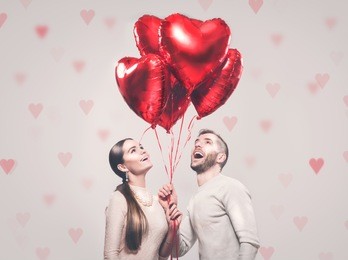 valentine couple. portrait of smiling beauty girl and her handsome boyfriend holding bunch of heart shaped air balloons and laughing. happy joyful family. love. happy valentine's day