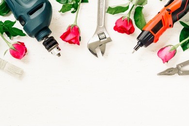flat lay of working construction tools and roses on grunge white wood. adjustable wrench, wrenches, paint brush, screwdriver, drill on white rustic wood background. valentines and labor day concept.