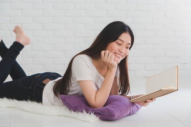 asian beautiful girl read a book on a pillow in a white room at home.smile face and feeling happy.