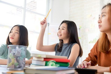 asian female oversea college student raising her hand asking question in the classroom while studying