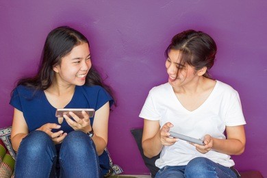 asian two young woman using mobile phone playing game, online shopping or   serving internet  together in relax time.