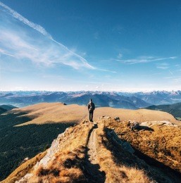 young man hiker stands back to camera on a cliff at the mountains dolomites and views of the valley, italy, seceda. traveler enjoy landscape