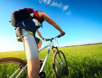 young man riding on a bicycle on green meadow with a red backpack