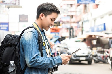 asian photographer tourist backpacker using tablet to find location while traveling on holiday in khao san road thailand