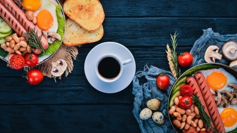 full english breakfast with fried eggs, sausages, beans, toasts and coffee on copy space background. on a black wooden background.