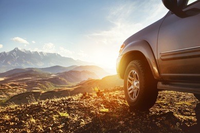 travel concept with big 4x4 car against sunset and mountains. closeup photo of offroad wheel
