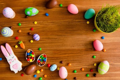 top view portrait with copy space for text of easter objects, on wooden brown background laying painted eggs, flower, baked cookies in carrot and hare figure