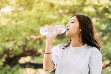 beautiful woman drinking water at summer green park. healthy lifestyle concept