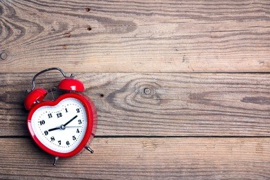 heart-shaped alarm clock  on old woooden background. place for text. top view. time for love and greetings.