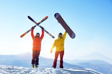 two active friends skier and snowboarder are standing on mountain top against blue sky and mountains. ski resort concept