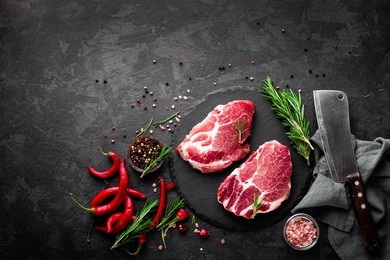 raw pork meat. fresh steaks on slate board on black background. top view