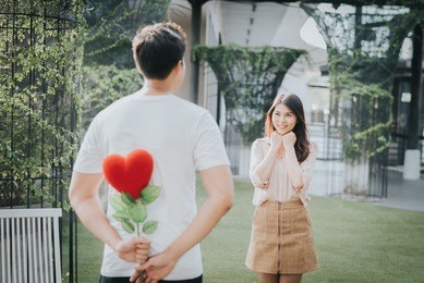 man holding heart shape flower behind the back to surprise his girlfriend in valentine day 