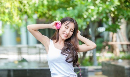 happy young beautiful girl listening to the music with her pink headphones and dancing in the urban park