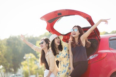 enjoying woman with her girlfriend traveler sitting on hatchback red car. summer vacation, holidays, travel, road trip and people concept .