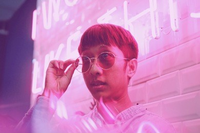 young asian hipster man in street style fashion summer concept and wearing sunglasses in pink neon light