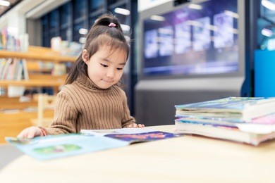 a little asian girl reading in the library