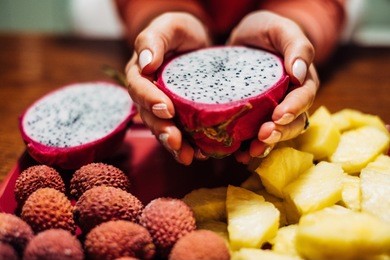 exotic fruits platter. pitahaya (dragon fruit), pineapple, lychees. woman hands holding fresh fruit. assorted made dish on plate on the table. summer healthy and tasty food.