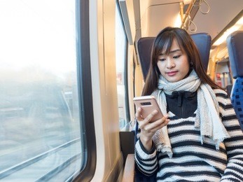 asian woman wearing striped sweater using her smartphone on german train  
