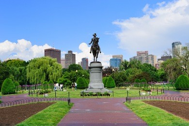 george washington statue as the famous landmark in boston common park with city skyline and skyscrapers.