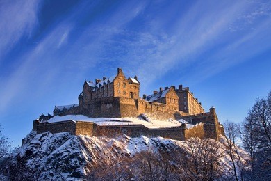 edinburgh castle dusted with snow glows in the late afternoon winter sunset.