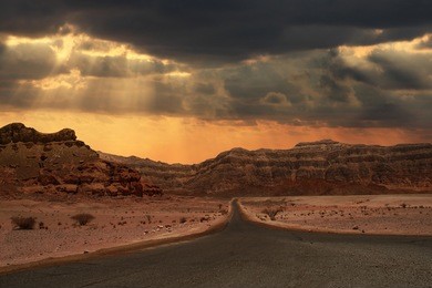 beautiful cloudy evening sky over narrow road running towards mountains of arava desert in israel.