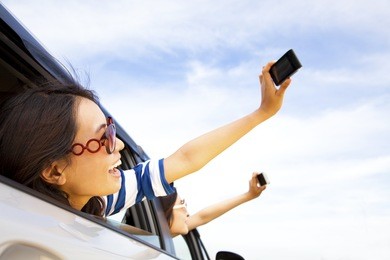 happy young woman  holding camera and mobile phone taking photos in the car